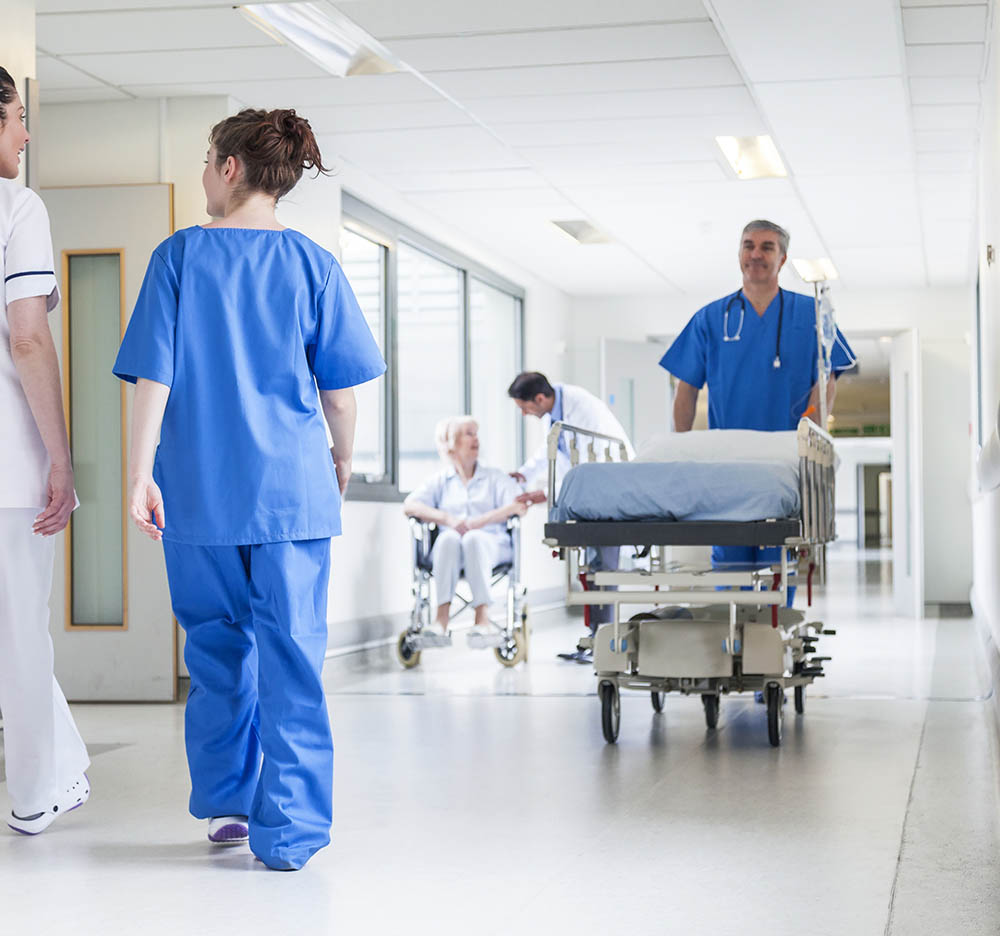 Male nurse pushing stretcher gurney bed in hospital corridor with doctors & senior female patient