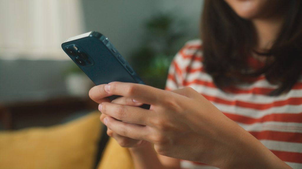 Close up of young person sit on sofa hand holding mobil