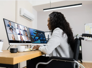 A black woman in a wheelchair attending an online meeting on one scree, with data on another screen.