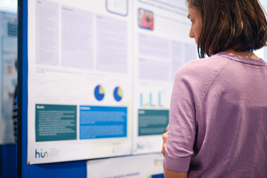 A woman with short hair is reading the South London Perinatal Optimisation Project case study posters displayed.