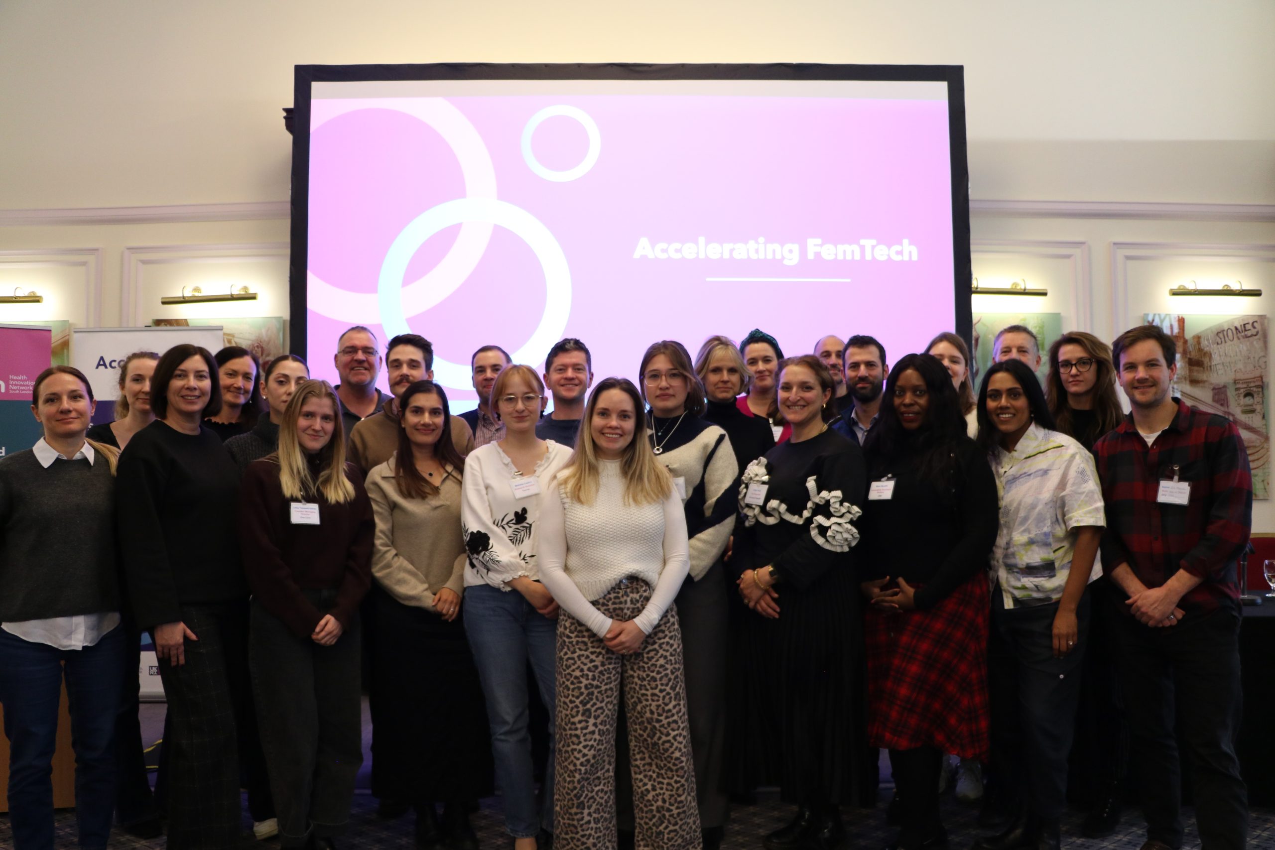 Group photo of a crowd of people. In the background is a projected slide, which displays the text 'Accelerating FemTech'