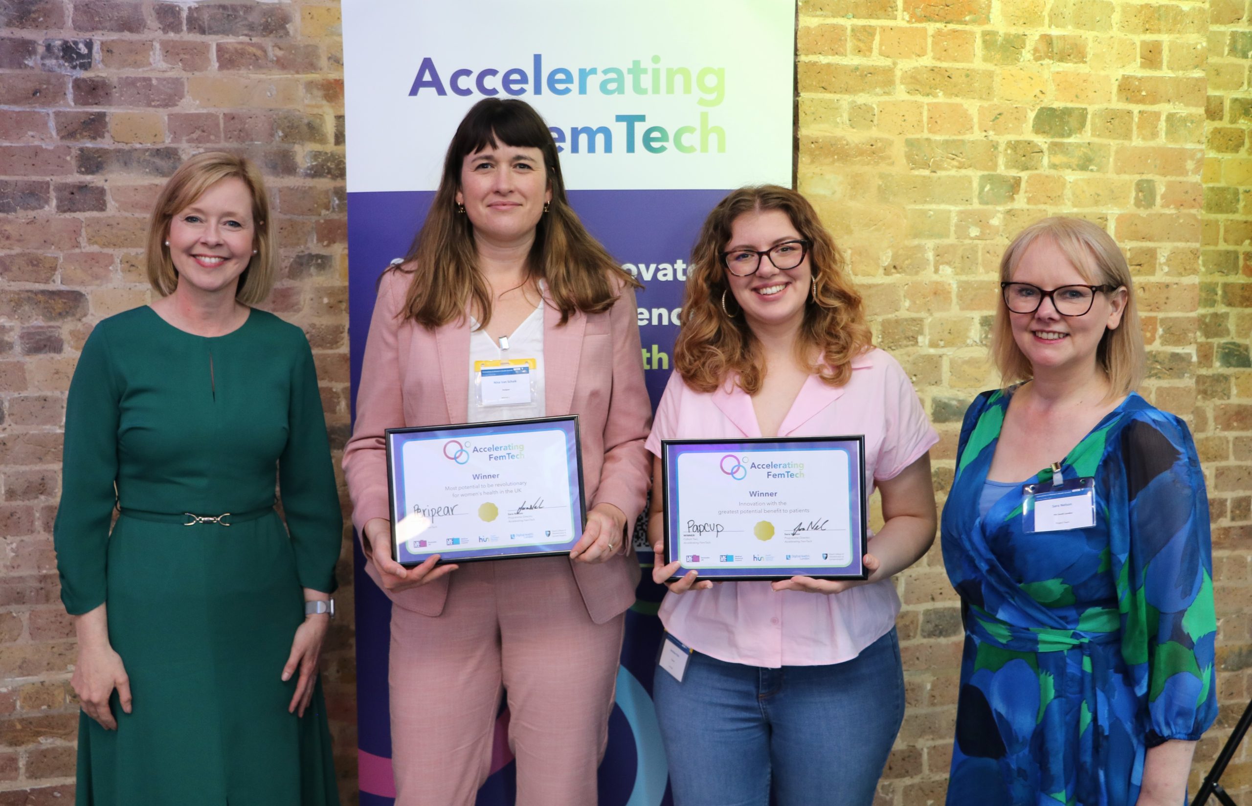 Four people stand in a row. Two people in the middle hold framed certificates.
