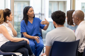 Clinician is with a group of people sat in chairs in a circle. The clinician is speaking to the group.